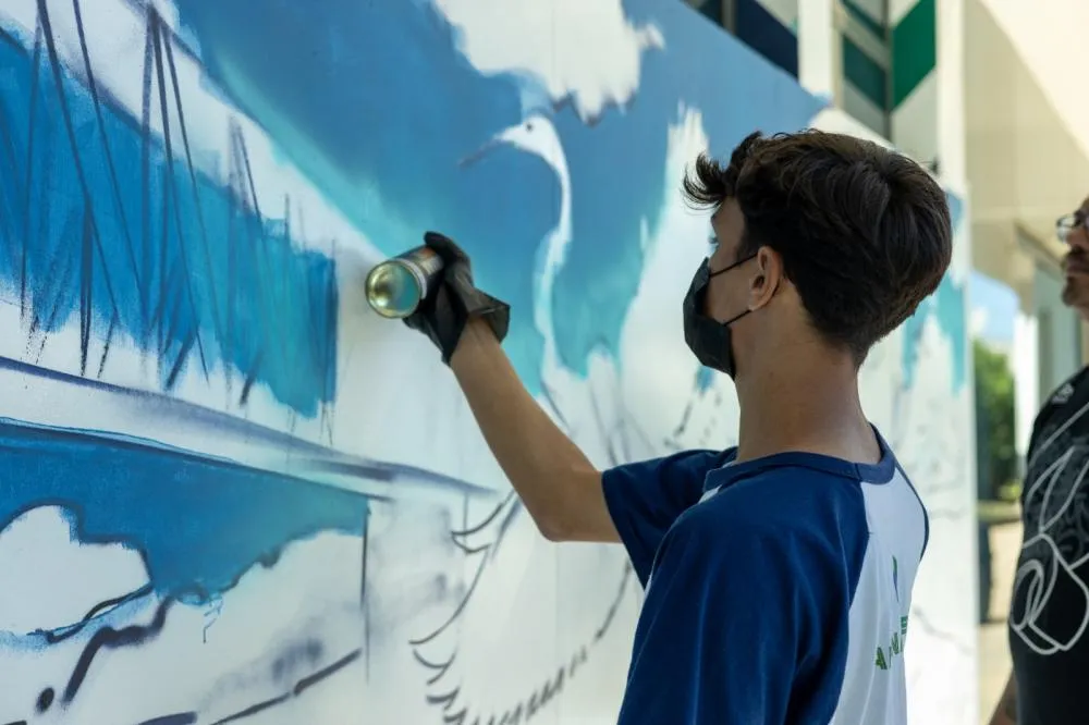 Jovens aprendem técnicas básicas de pintura com sprays durante oficina de grafite realizada em espaço público do Paraná. A ação é coordenada pelos Núcleos de Cooperação Socioambiental.